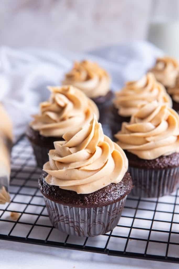 Chocolate cupcakes topped with piped peanut butter frosting on top of a wire cooling rack