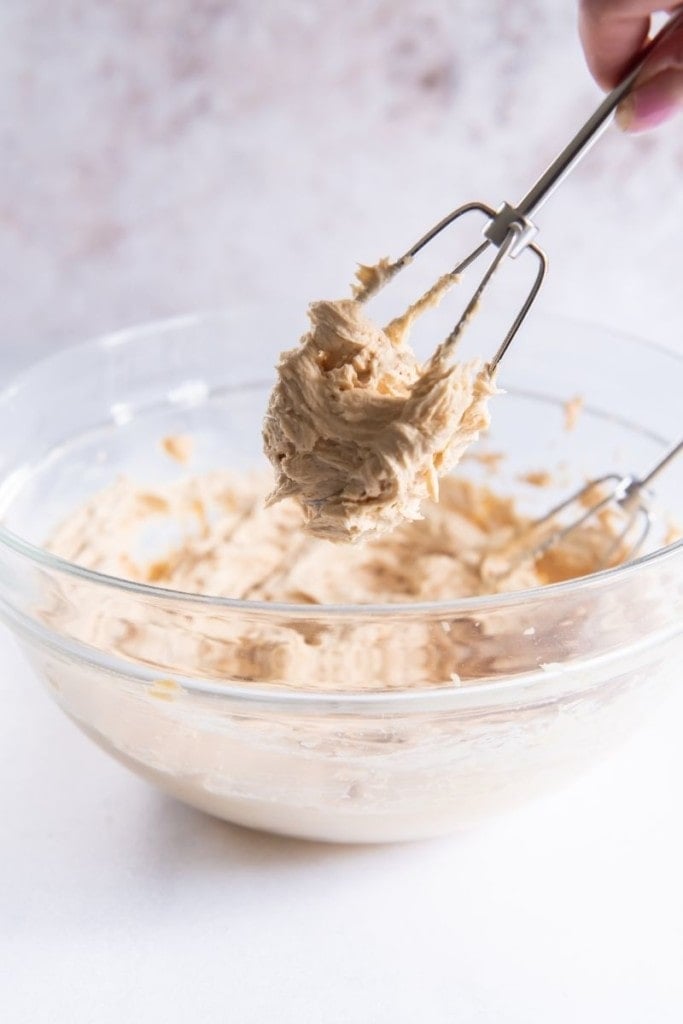Whipped peanut butter frosting on a whisk above a bowl of it