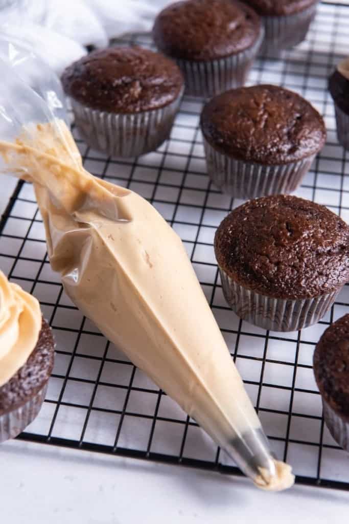 Piping bag with frosting next to chocolate cupcakes on a cooling rack