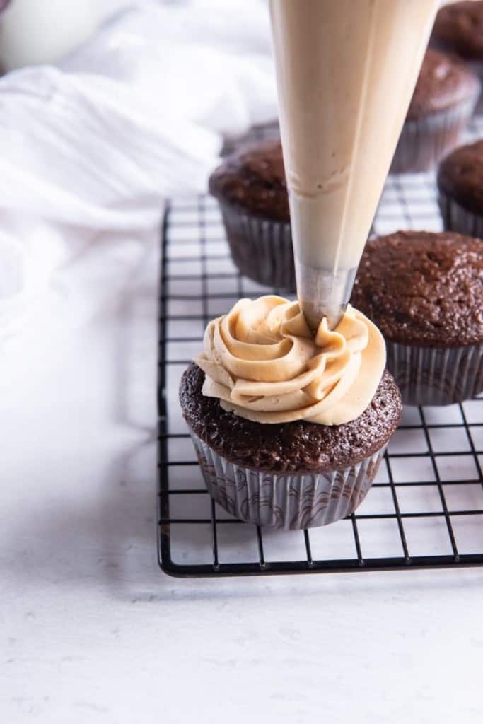 3 Ingredient Peanut Butter Frosting being piped onto a chocolate cupcake on top of a wire rack