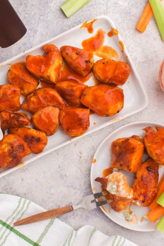 Air Fryer Boneless wings on a rectangle serving plate and some on a plate with fork inside one of the wings