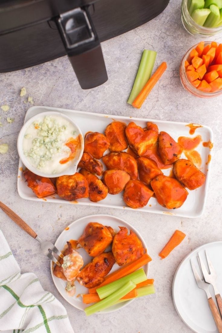 Air Fryer Boneless Wings on a rectangle serving platter covered with buffalo sauce and paired with blue cheese and carrots/celery