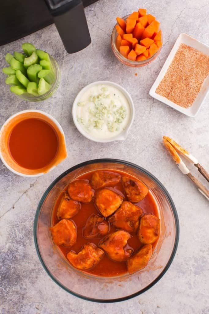 Boneless wings being tossed in buffalo sauce with blue cheese, celery, and carrots around it
