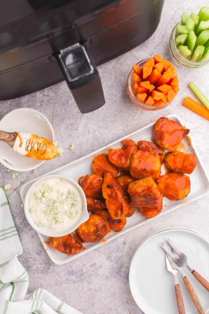 Boneless wings on a rectangle platter served with blue cheese, carrots, and celery in front of an air fryer