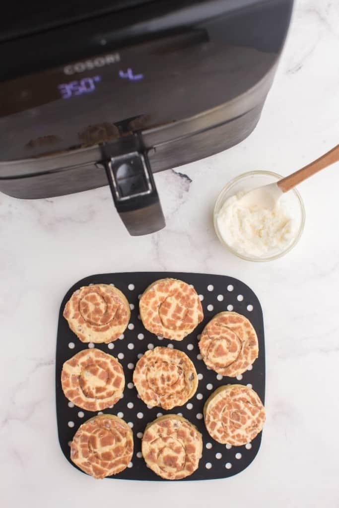 Cinnamon Rolls in front of an air fryer on a black silicone liner