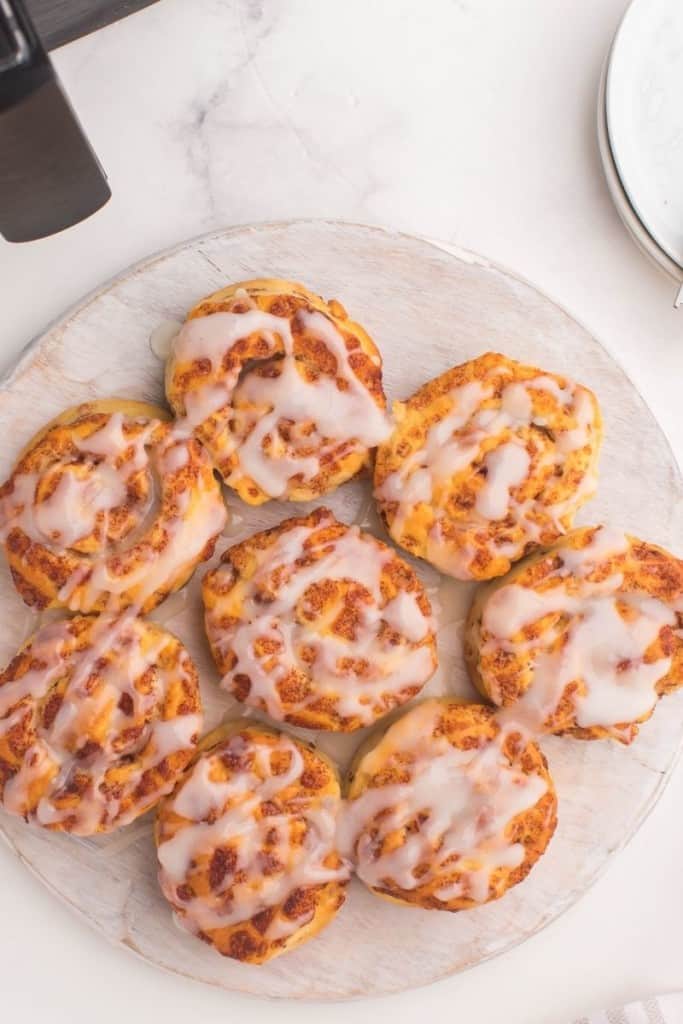 Air Fryer Cinnamon Rolls with icing on them on top of a round white plate