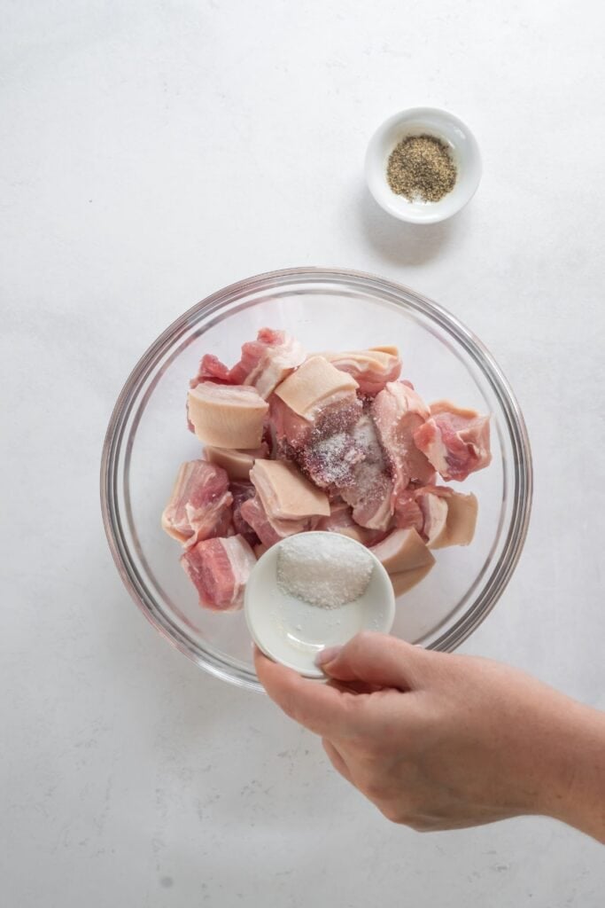 Pork belly in a bowl with salt about to be poured onto it.