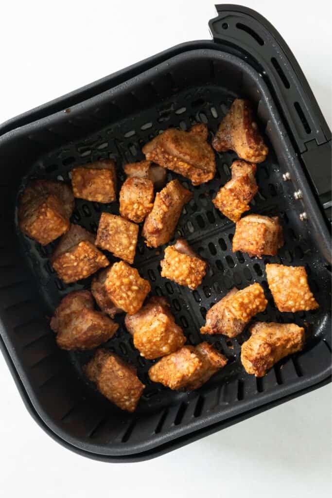 Cooked pork belly in an air fryer basket that is golden brown and crispy.