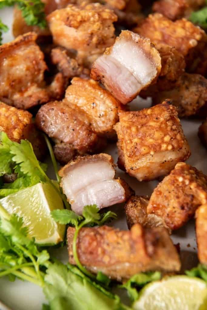 Crispy Air Fryer Pork Belly bites ona plate with greens and lime