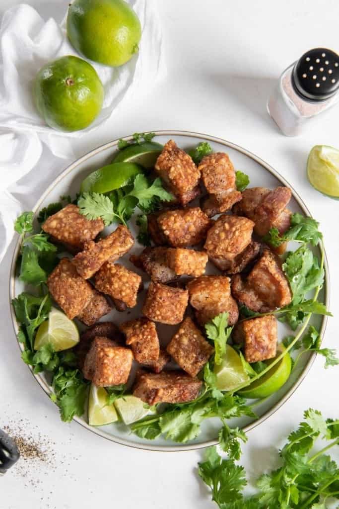 Air Fryer Pork Belly Bites on a plate covered in green garnishes and limes