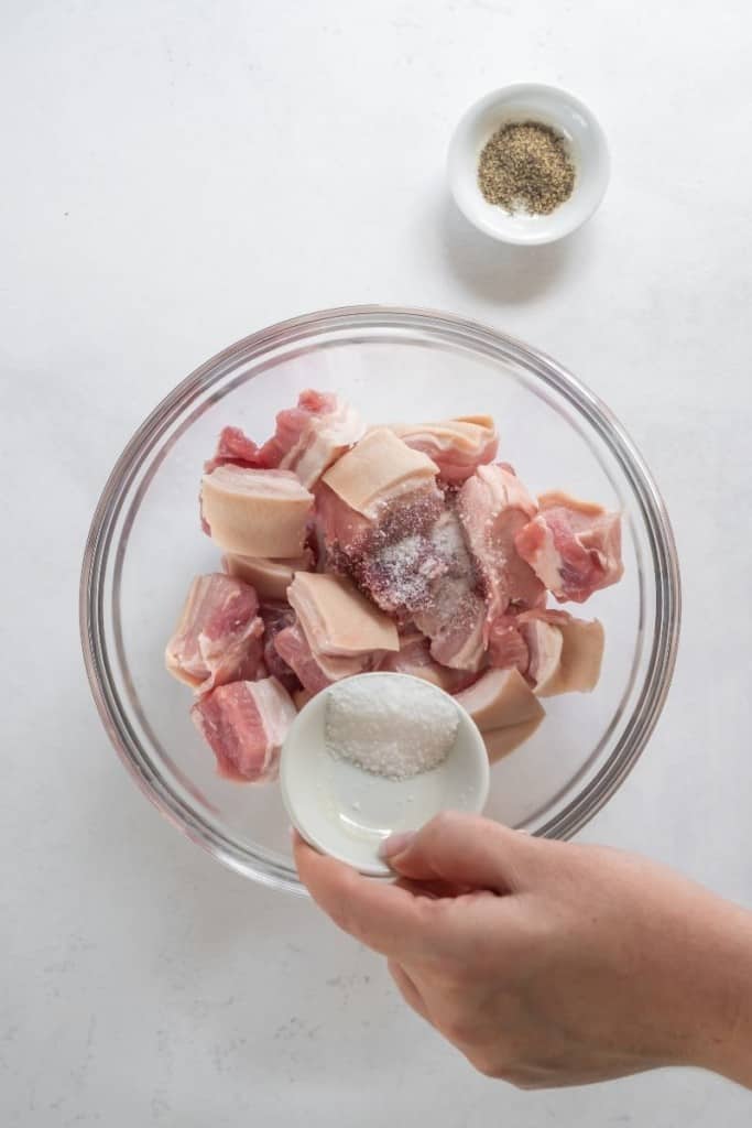 Pork belly in a bowl with salt and pepper being sprinkled over it