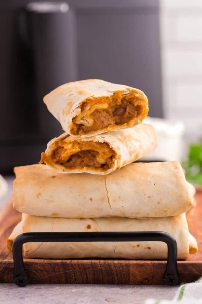 Burritos stacked on top of each other on a wooden serving plate with top two pieces cut in half