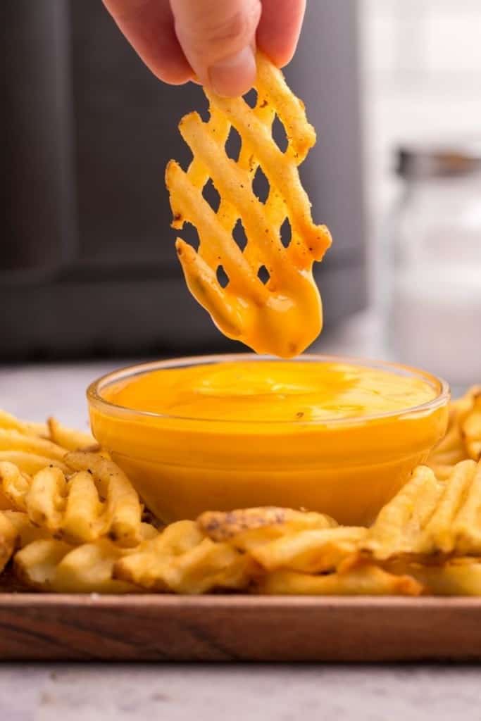 Waffle fry being dipped into nacho cheese
