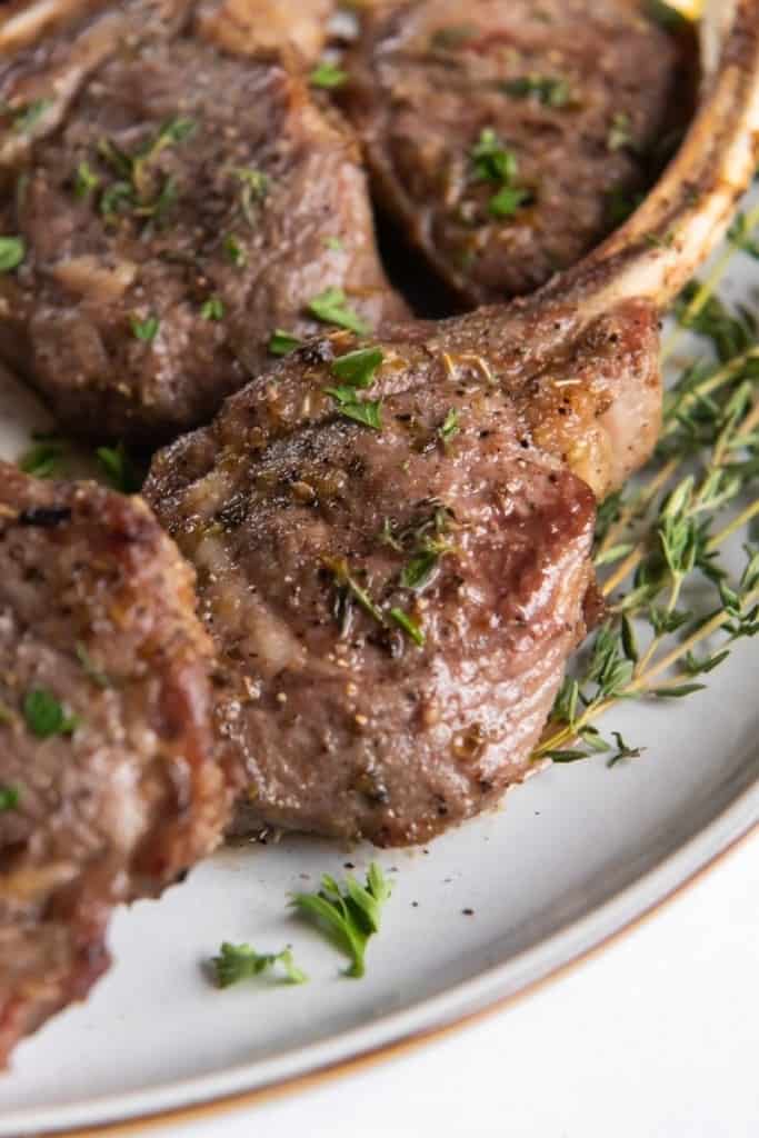 Closeup of air fryer lamb chops on a white plate with garnishes