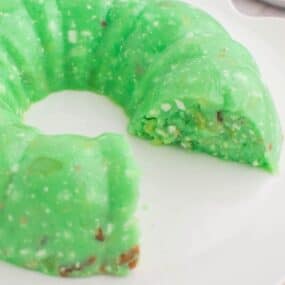 Lime Jello Salad with Cottage Cheese made in a bundt pan and flipped onto a white plate with piece cut out and missing