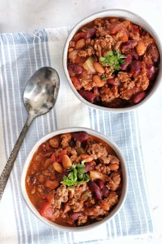 Two bowls of chili topped with a little cilantro with a cloth napkin and spoon 