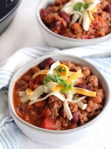 Closeup of a bowl of chili topped with shredded cheese and some cilantro