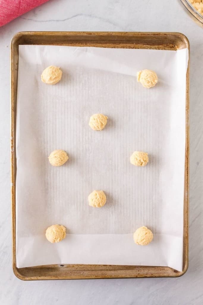 Rolled raw cookies on a cookie sheet with parchment paper