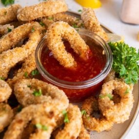 Air Fryer Calamari rings served on a white plate with cocktail sauce and one being dipped into it
