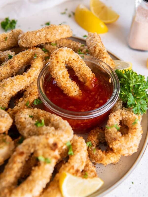 Air Fryer Calamari rings served on a white plate with cocktail sauce and one being dipped into it