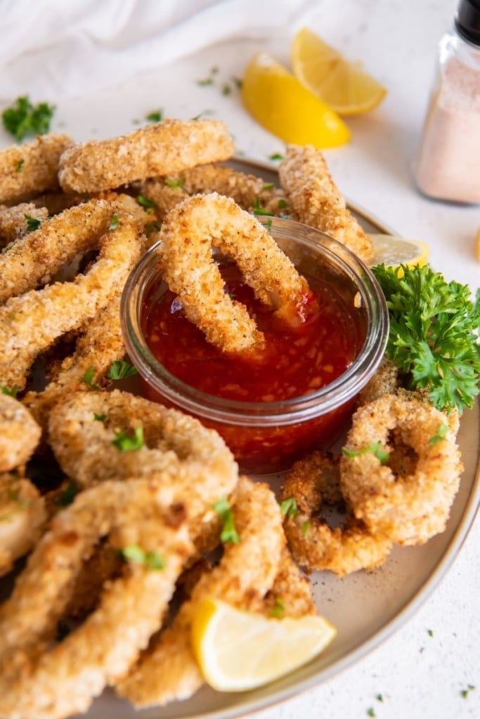 Air Fryer Calamari rings served on a white plate with sweet chili sauce and one being dipped into it