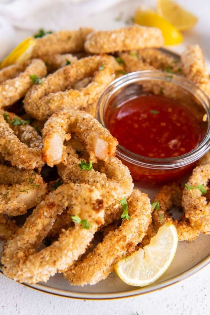 Breaded calamari rings on a serving plate with sweet chili sauce and one broken in half to see the inside