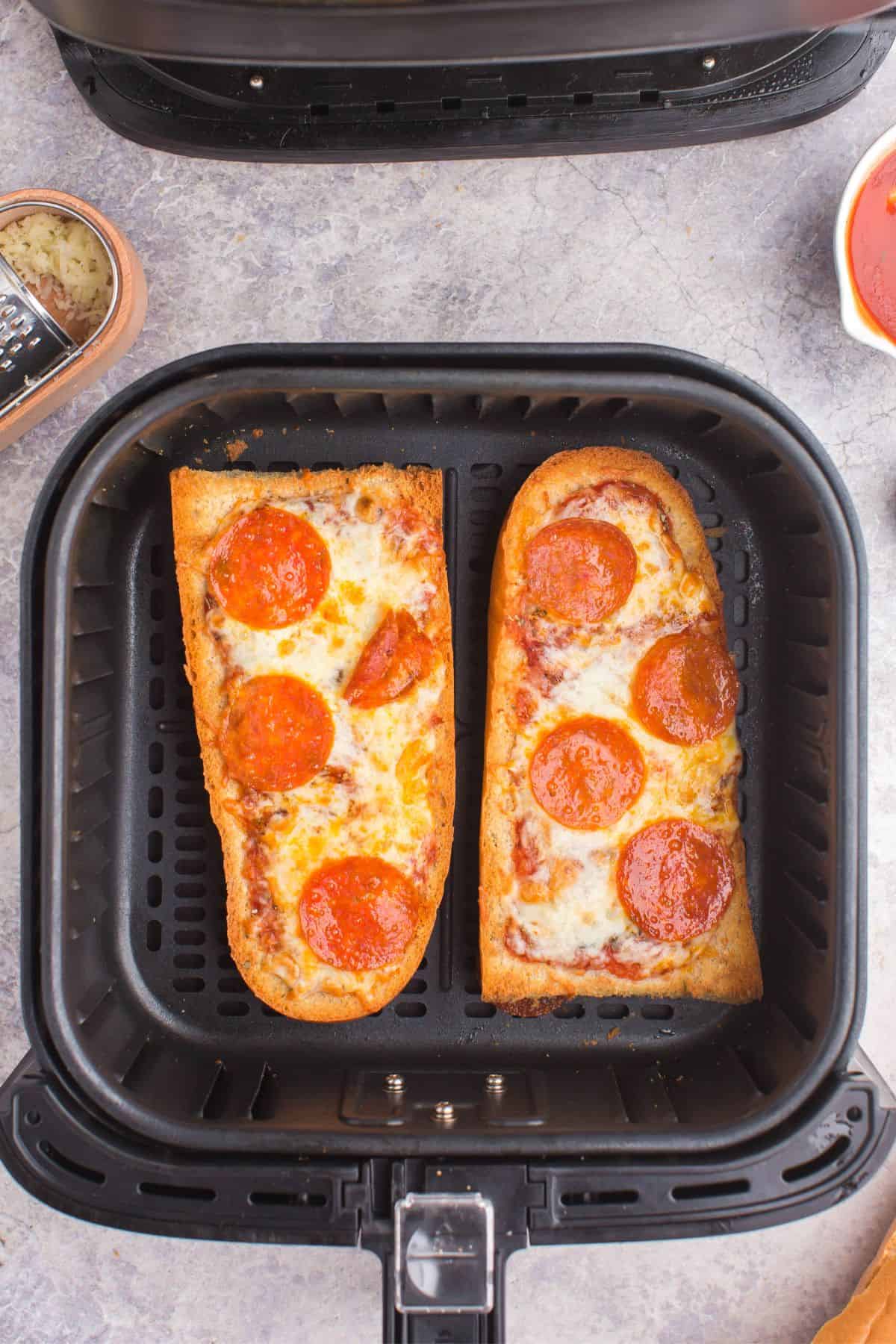 Melted cheese and pepperoni on the air fryer french bread pizza in the air fryer basket.