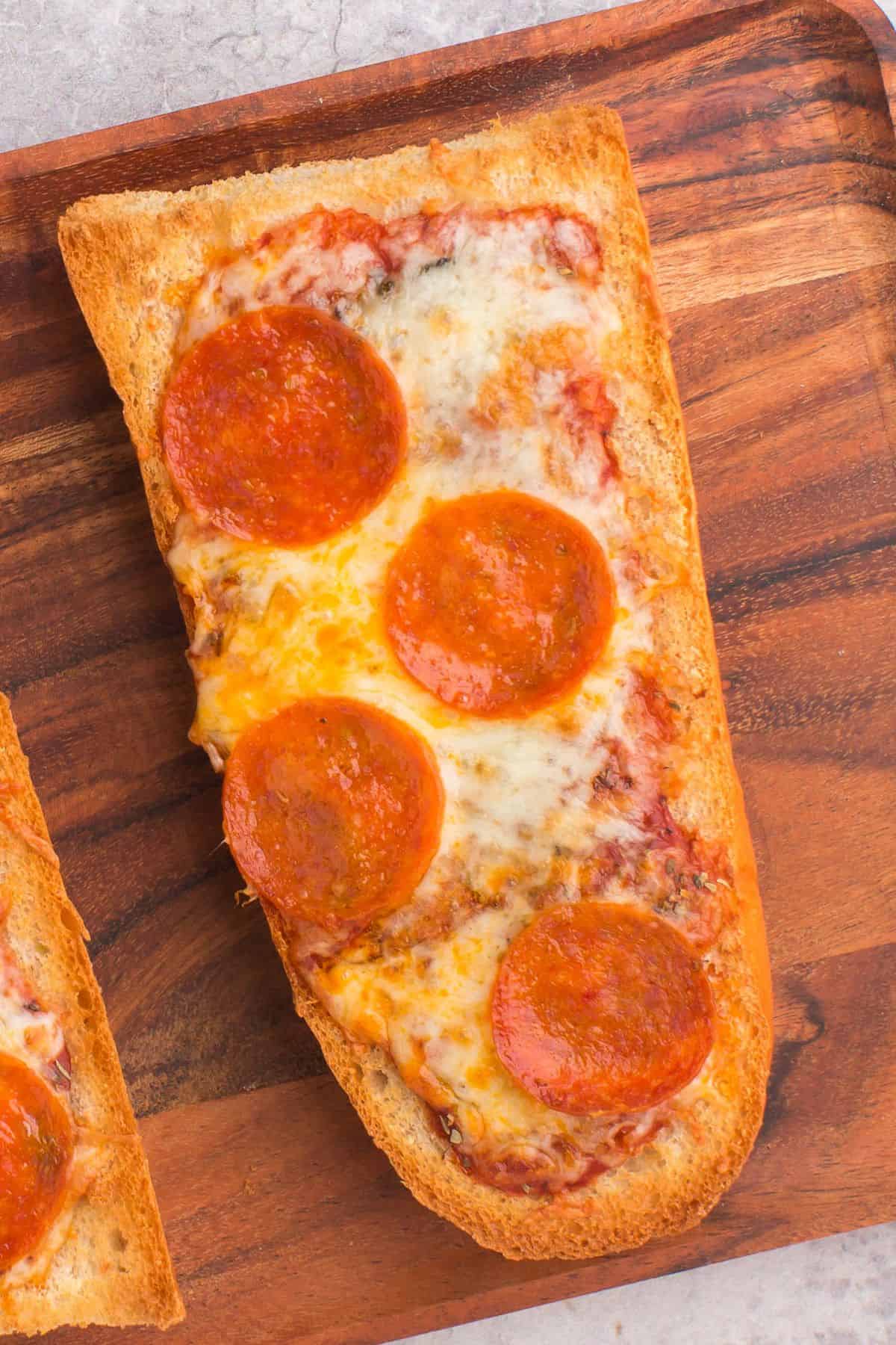 Air fryer french bread pizza with pepperoni on a wooden serving tray.
