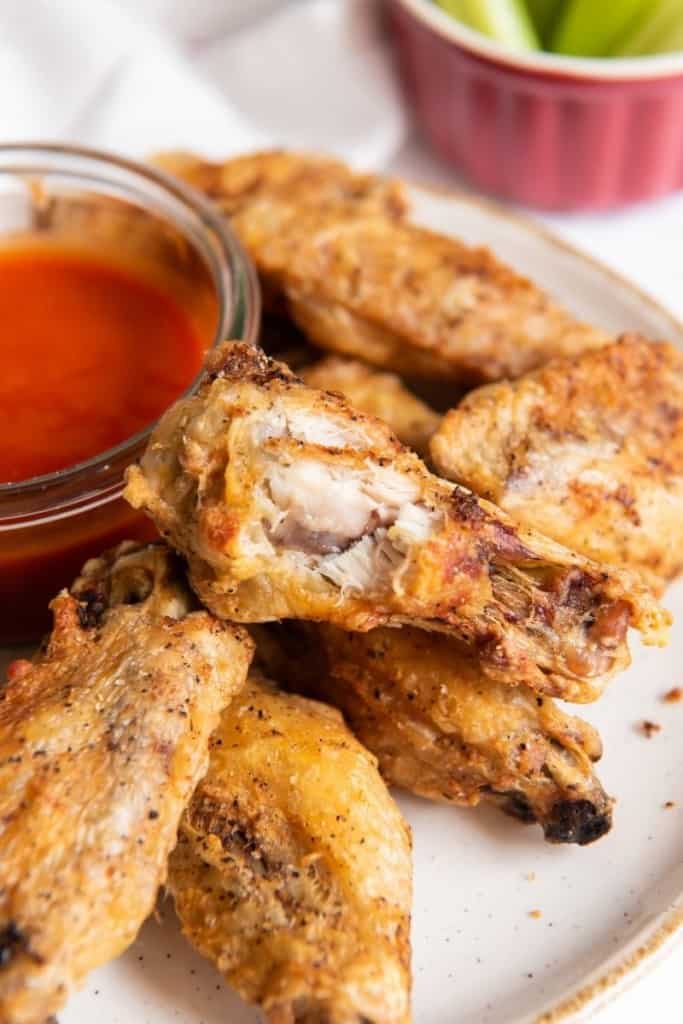 Chicken wings on a plate with buffalo sauce in a bowl and chicken wing with a bite taken out of it