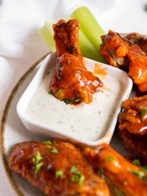 Air Fryer Frozen Chicken Wings coated with buffalo sauce on a white plate with one drumstick being dipped into blue cheese
