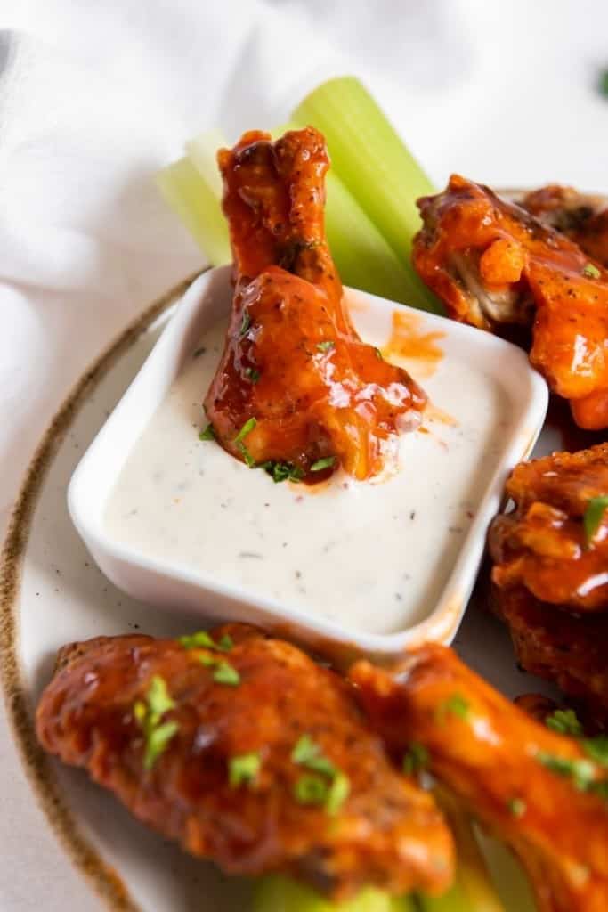Air Fryer Frozen Chicken Wings coated with buffalo sauce on a white plate with one drumstick being dipped into blue cheese
