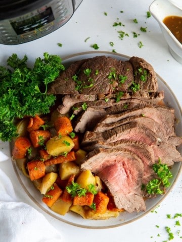 Instant Pot Sirloin Roast with carrots and potatoes on a plate with parsley next to an Instant Pot