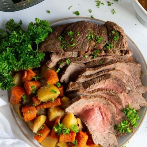 Instant Pot Sirloin Roast with carrots and potatoes on a plate with parsley next to an Instant Pot