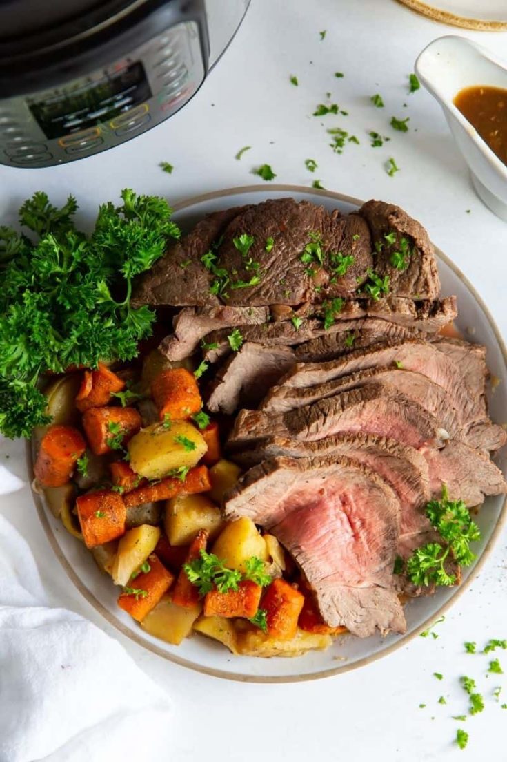 Instant Pot Sirloin Roast with carrots and potatoes on a plate with parsley next to an Instant Pot
