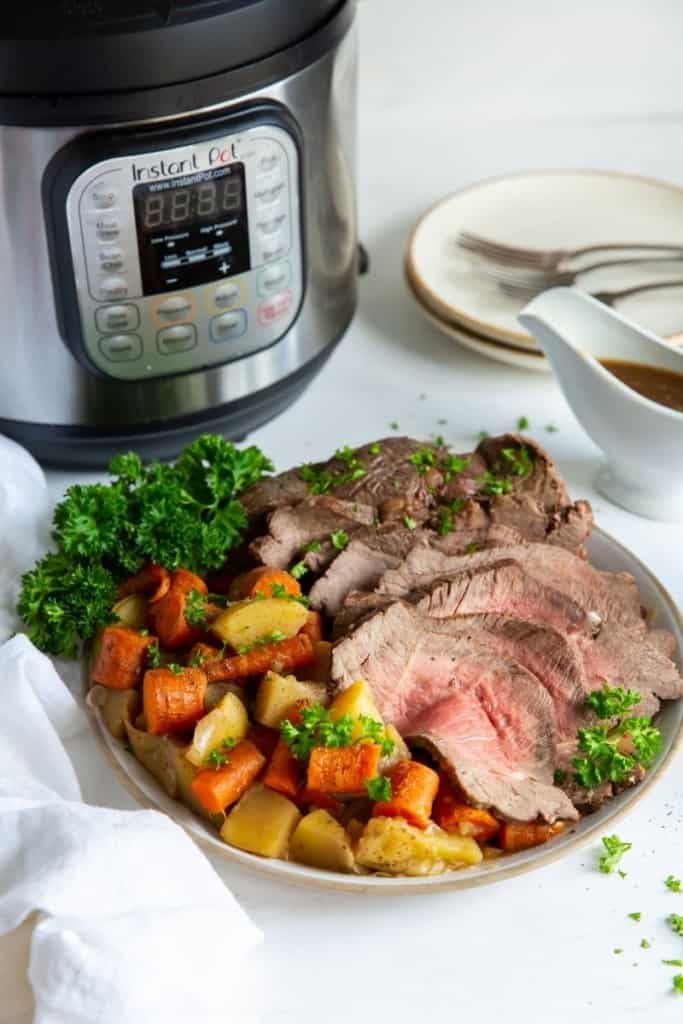 Sirloin tip roast with vegetables on a plate in front of an Instant Pot