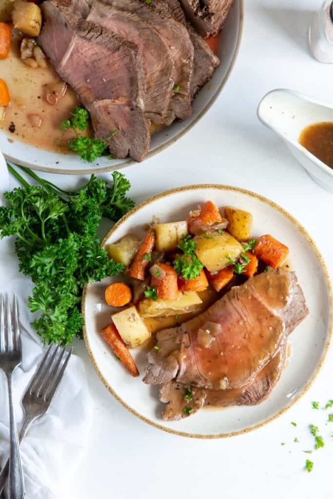 Plated instant pot roast on a plate with carrots and potatoes with serving plate in background