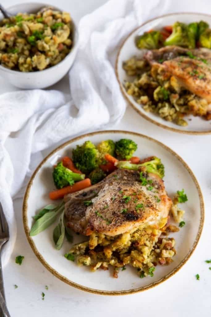 Air Fryer Stuffed Pork Chops on a plate served with veggies and a bowl of extra stuffing in the background