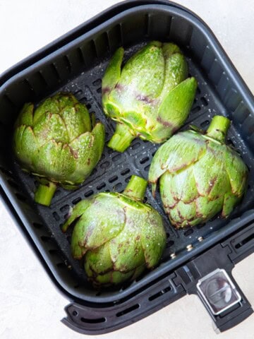 Artichokes in the air fryer basket with cut side down.