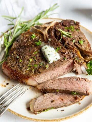 air fryer t bone steak on a white plate, cut into.