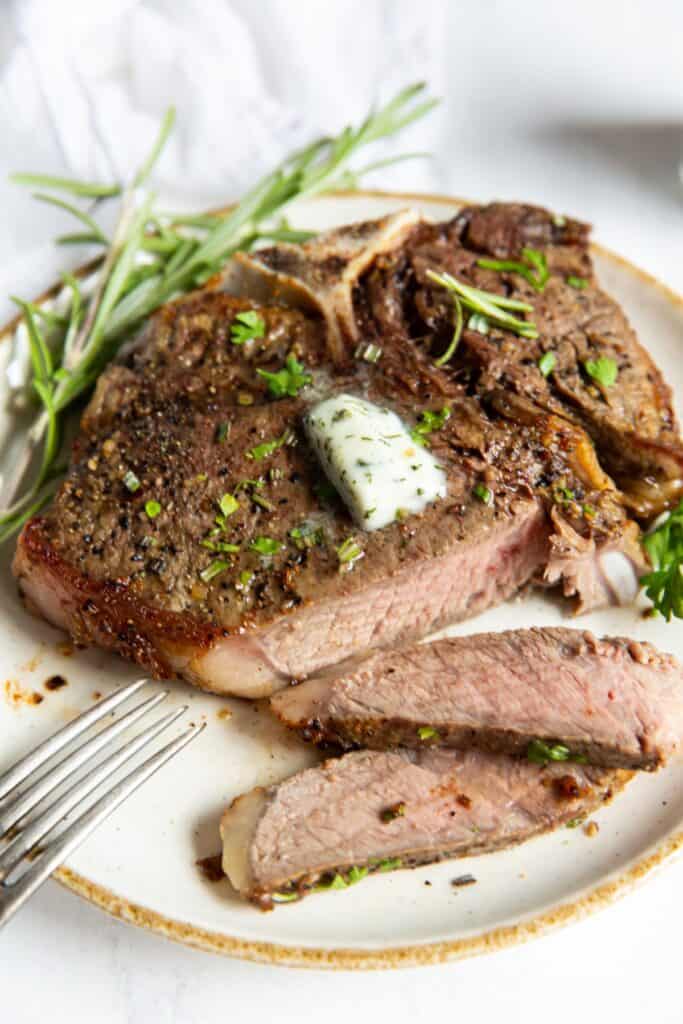 air fryer t bone steak on a white plate, cut into.