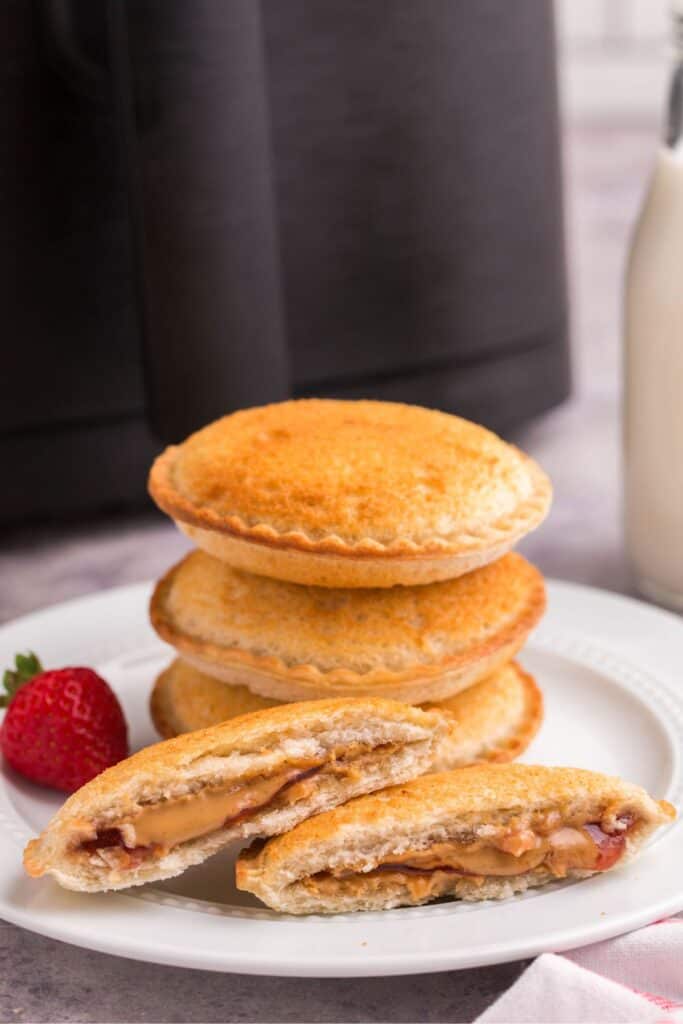 Uncrustables that were cooked in the air fryer stacked on each other with one split in half in front of them.