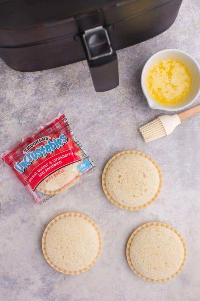 Uncrustable packaging and product on the counter with an air fryer and butter.