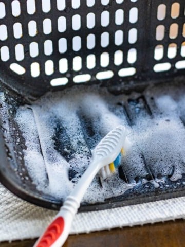 Toothbrush cleaning an air fryer with Dawn Powerwash Spray