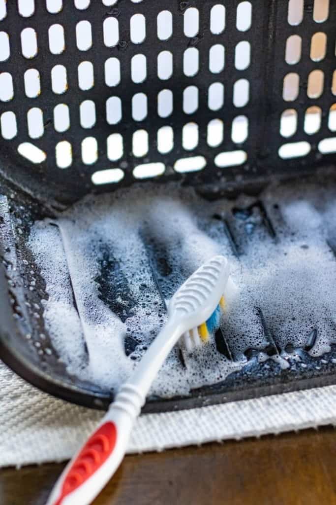 Toothbrush cleaning an air fryer with Dawn Powerwash Spray