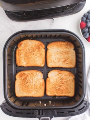 4 pieces of toast in an air fryer basket with perfect golden brown on top.