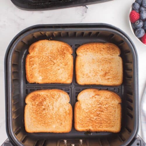 4 pieces of toast in an air fryer basket with perfect golden brown on top.