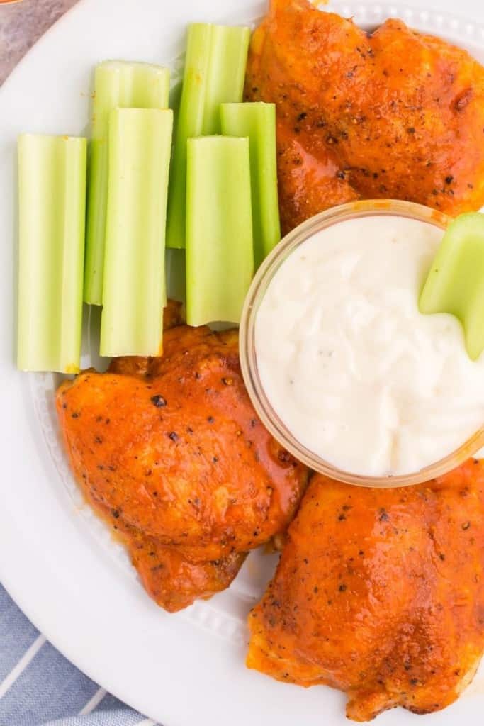 buffalo chicken thighs on plate with celery sticks and dipping sauce