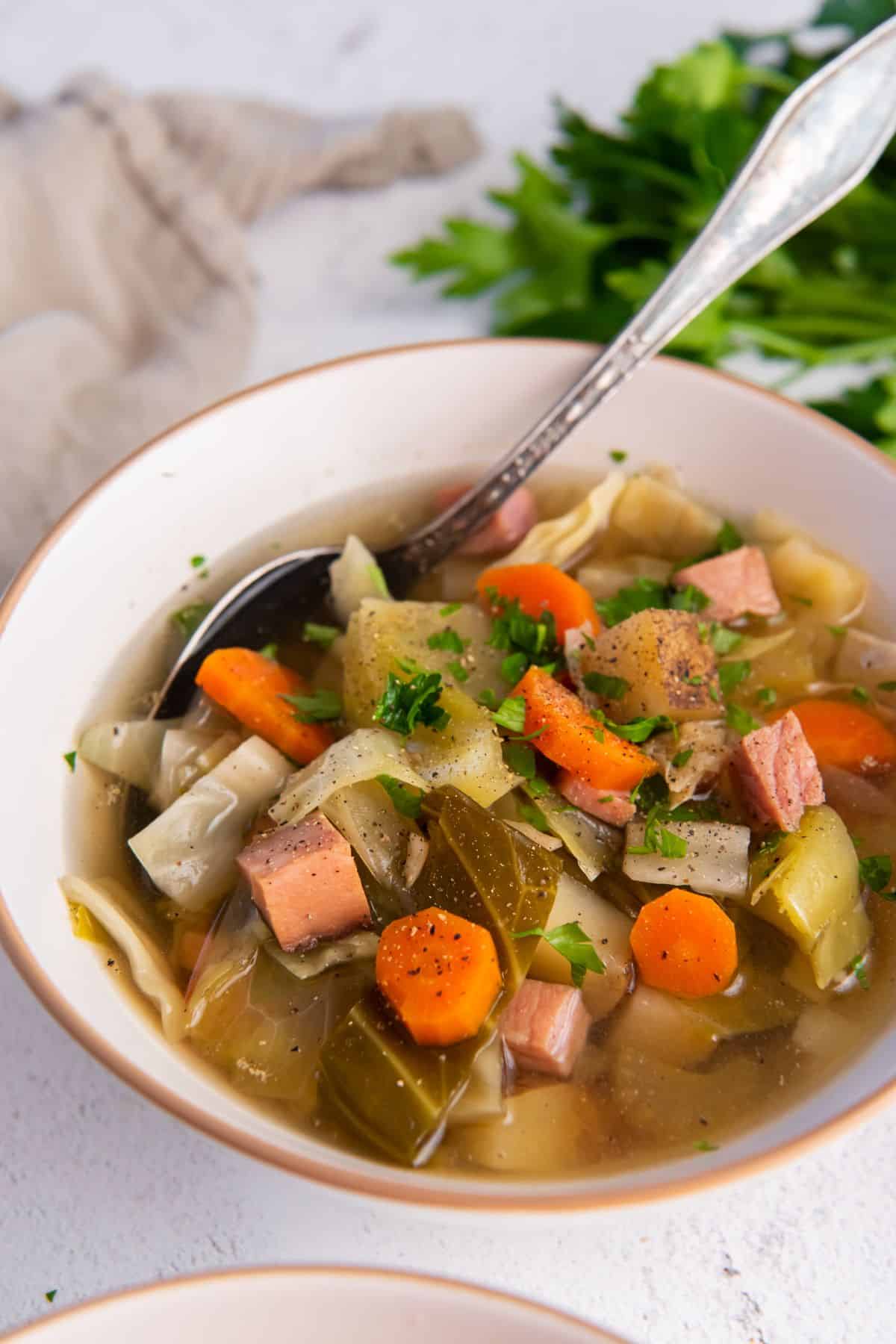 Crockpot ham and cabbage soup in a white bowl with a spoon.