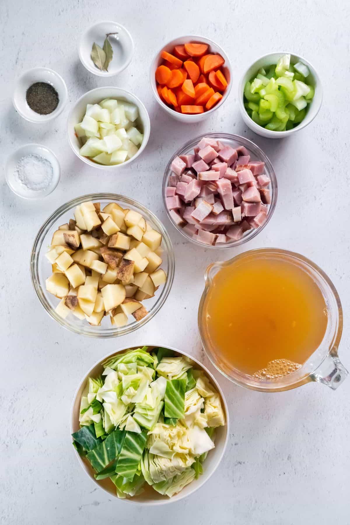 Ingredients needed to make crockpot ham and cabbage: potatoes, cabbage, onion, carrots, celery, ham, bay leaves, salt, pepper, chicken broth, and parsley.