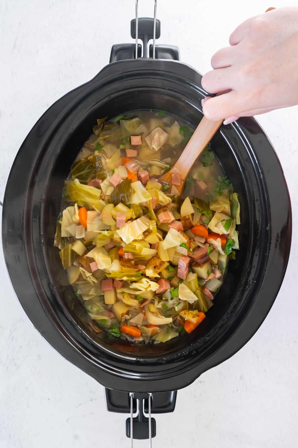 ham and cabbage soup in the slow cooker being stirred after cooking.